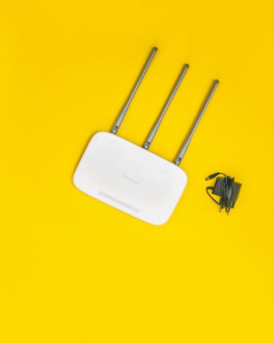 White router with three antennas and cables on bold yellow background, ideal for tech concepts.